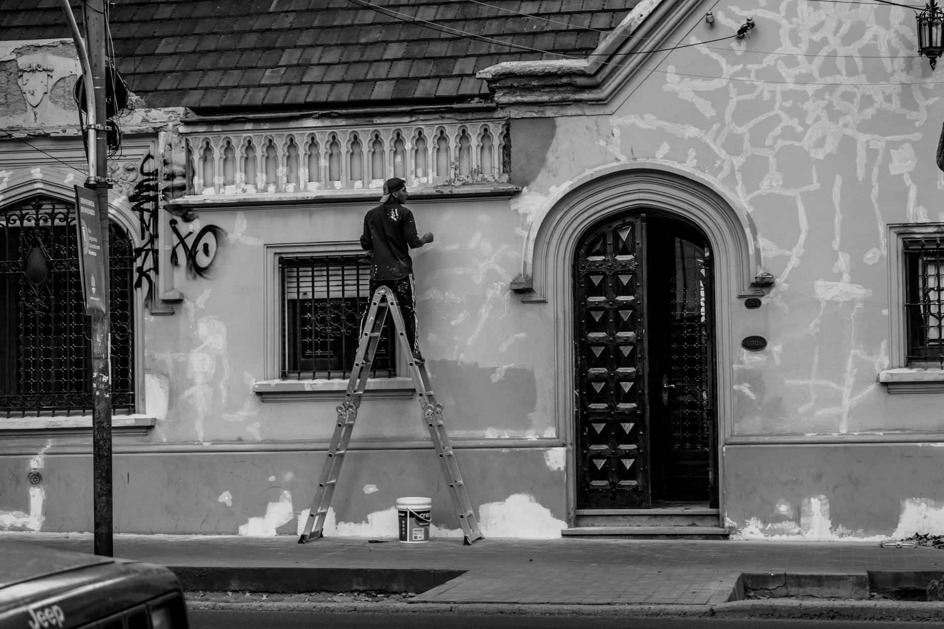 Pintor profesional aplicando pintura blanca en paredes de un salón luminoso y reformado
