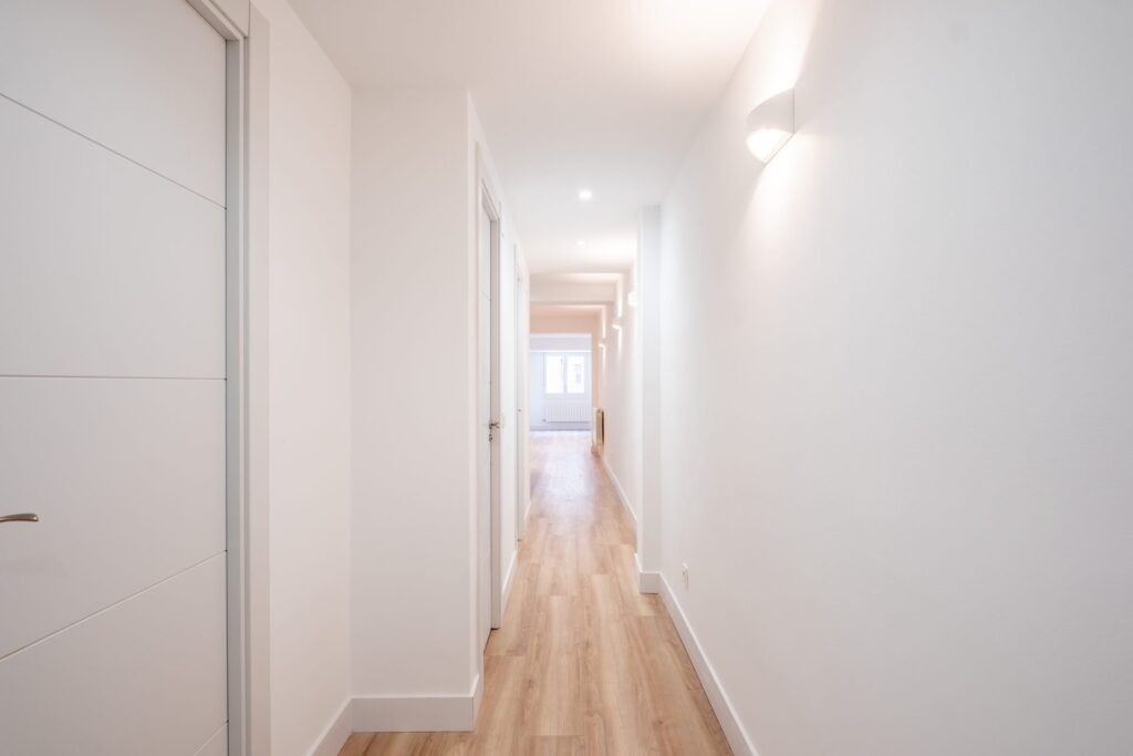 Pasillo reformado con suelo de madera y puertas lacadas blancas